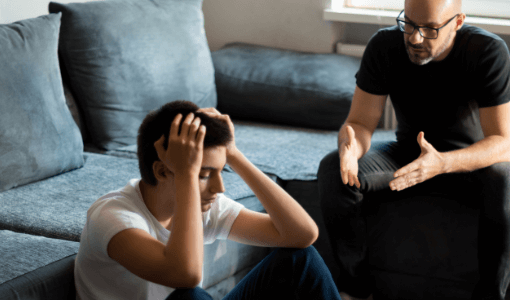 Un adulte s'adresse à un adolescent qui est assis, les yeux baissés et qui tient sa tête entre les mains.