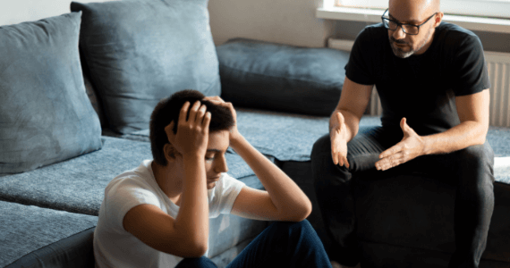 Un adulte s'adresse à un adolescent qui est assis, les yeux baissés et qui tient sa tête entre les mains.